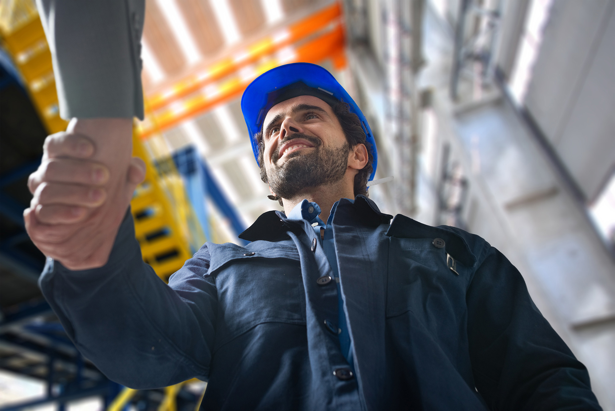 Construction worker in blue hard hat smiling and shaking hands indoors.
