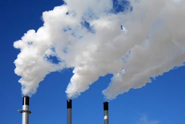 三根工业烟囱在晴朗的蓝天下排放白烟。