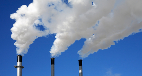 Three industrial chimneys emitting white smoke against a clear blue sky.