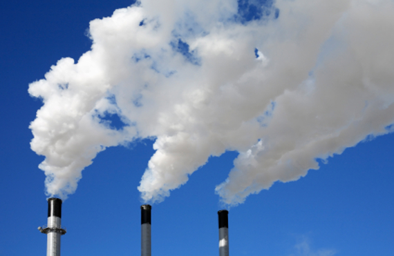 Three industrial chimneys emitting white smoke against a clear blue sky.
