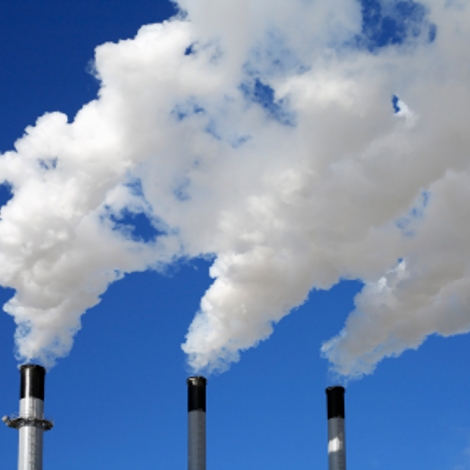 Three industrial chimneys emitting white smoke against a clear blue sky.