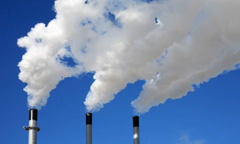 Three industrial chimneys emitting white smoke against a clear blue sky.