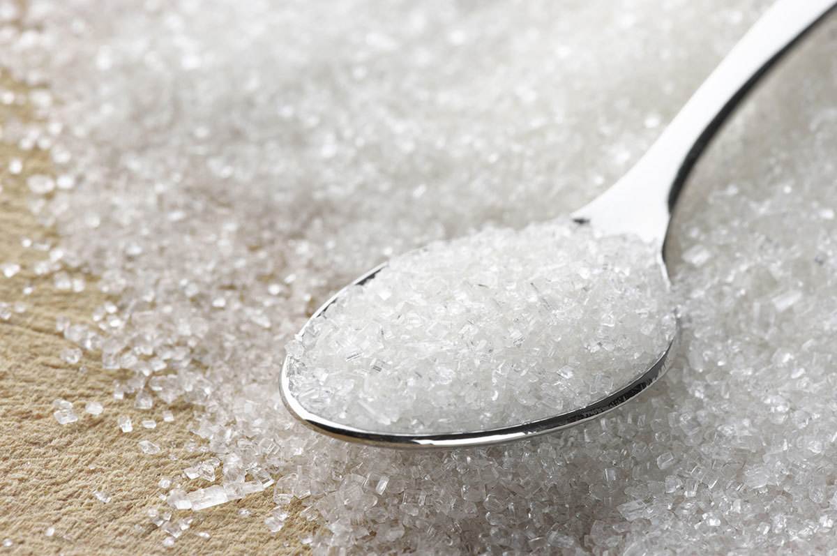Close-up of a spoon filled with white granulated sugar on a wooden surface.