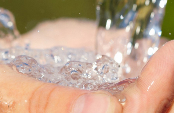 Hands cupped under flowing water against a blurred natural background.