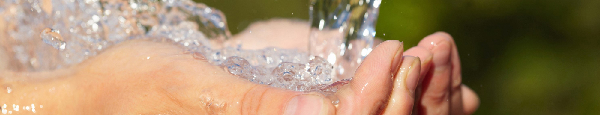 Manos ahuecadas bajo agua corriente contra un fondo natural desenfocado.