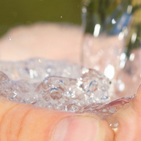 Hands cupped under flowing water against a blurred natural background.