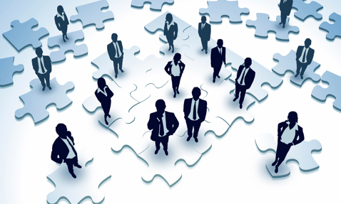 Silhouetted businesspeople standing on large puzzle pieces, symbolizing teamwork and collaboration.
