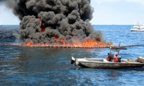 Boat near a controlled burn of an oil spill at sea.