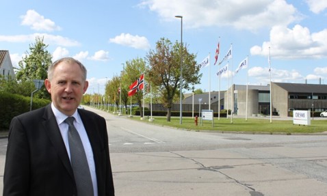 穿西装的男子站在DESMI大楼外，背景是旗帜和多云的天空。