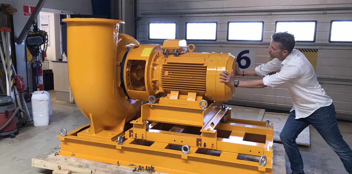 Hombre empujando una gran bomba industrial amarilla dentro de un taller.