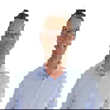 Smiling man in glasses and a light blue shirt against a white background.