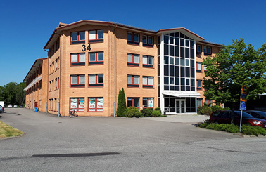 Brick building with large windows and number 34, surrounded by trees and parking.