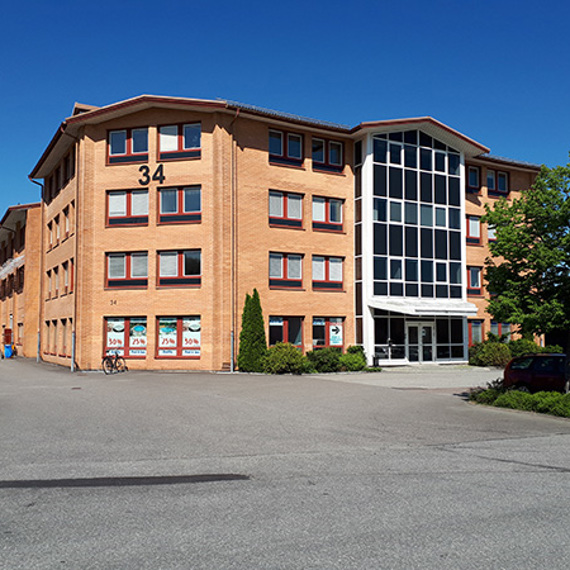 Brick building with large windows and number 34, surrounded by trees and parking.