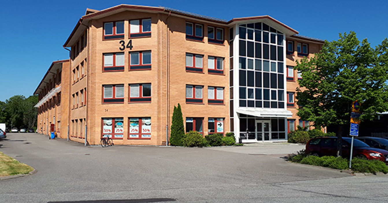 Brick building with large windows and number 34, surrounded by trees and parking.
