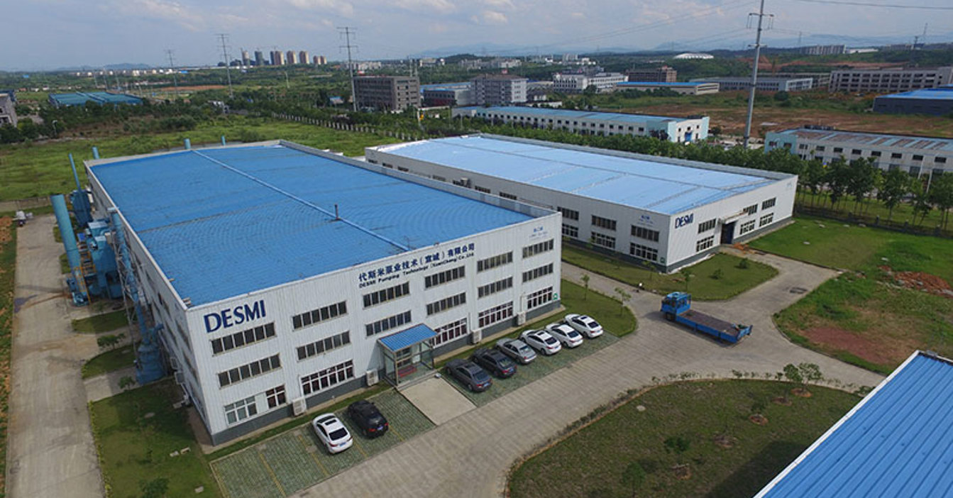 Aerial view of DESMI facility with blue-roofed buildings and surrounding greenery.