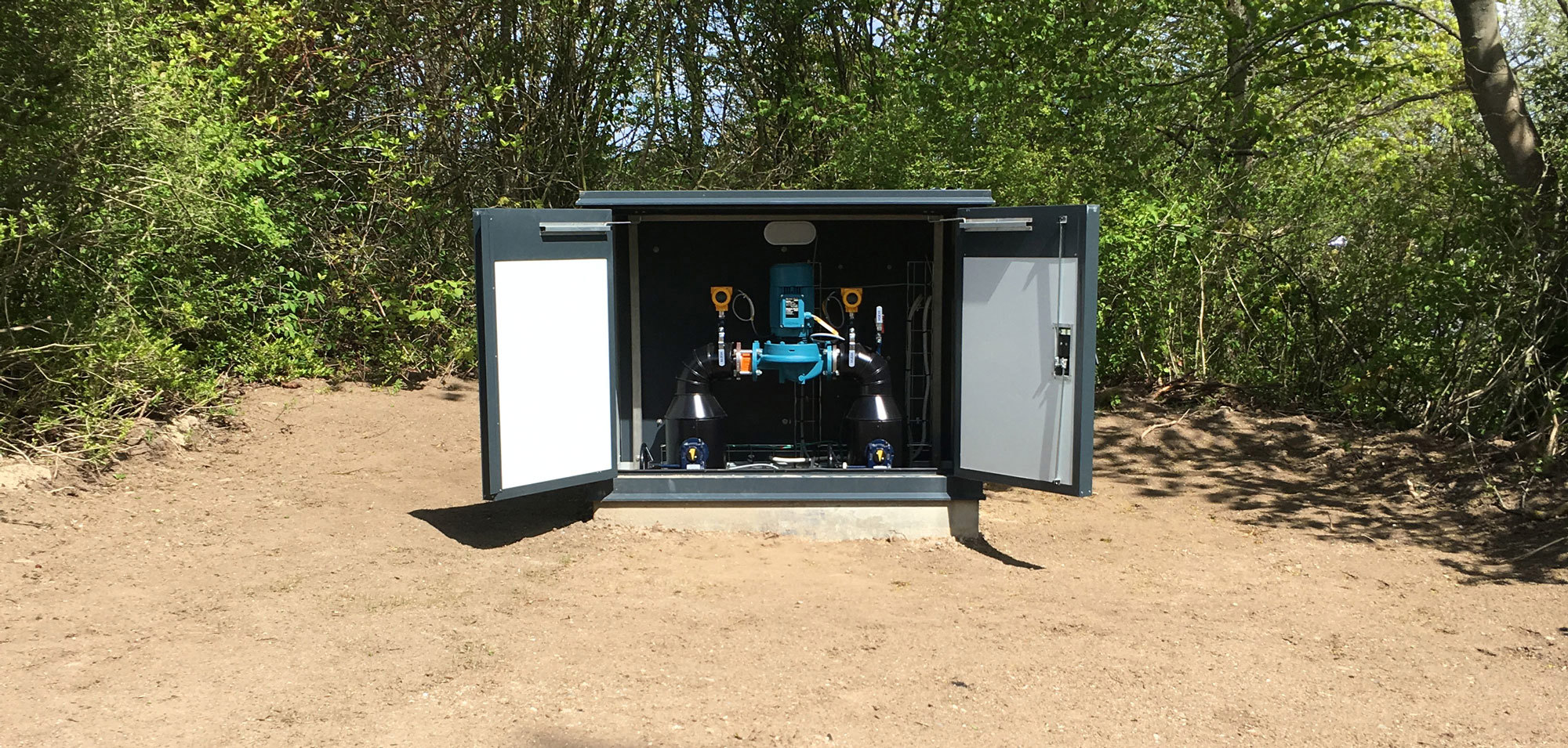DESMI pump system installed in an outdoor cabinet surrounded by trees.