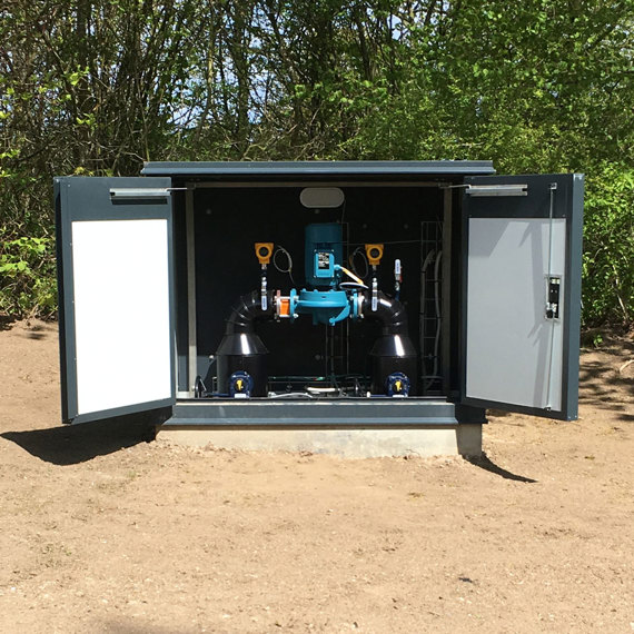 DESMI pumpsystem installerat i ett utomhusskåp omgivet av träd.