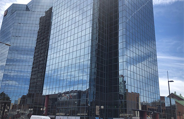 Modern glass skyscraper reflecting the blue sky and surrounding buildings.