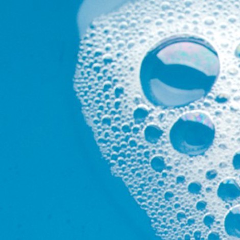 Bańki mydlane unoszące się na niebieskiej wodzie, ukazujące opalizujące kolory.