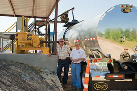 Two men standing near industrial equipment and a shiny tanker truck.