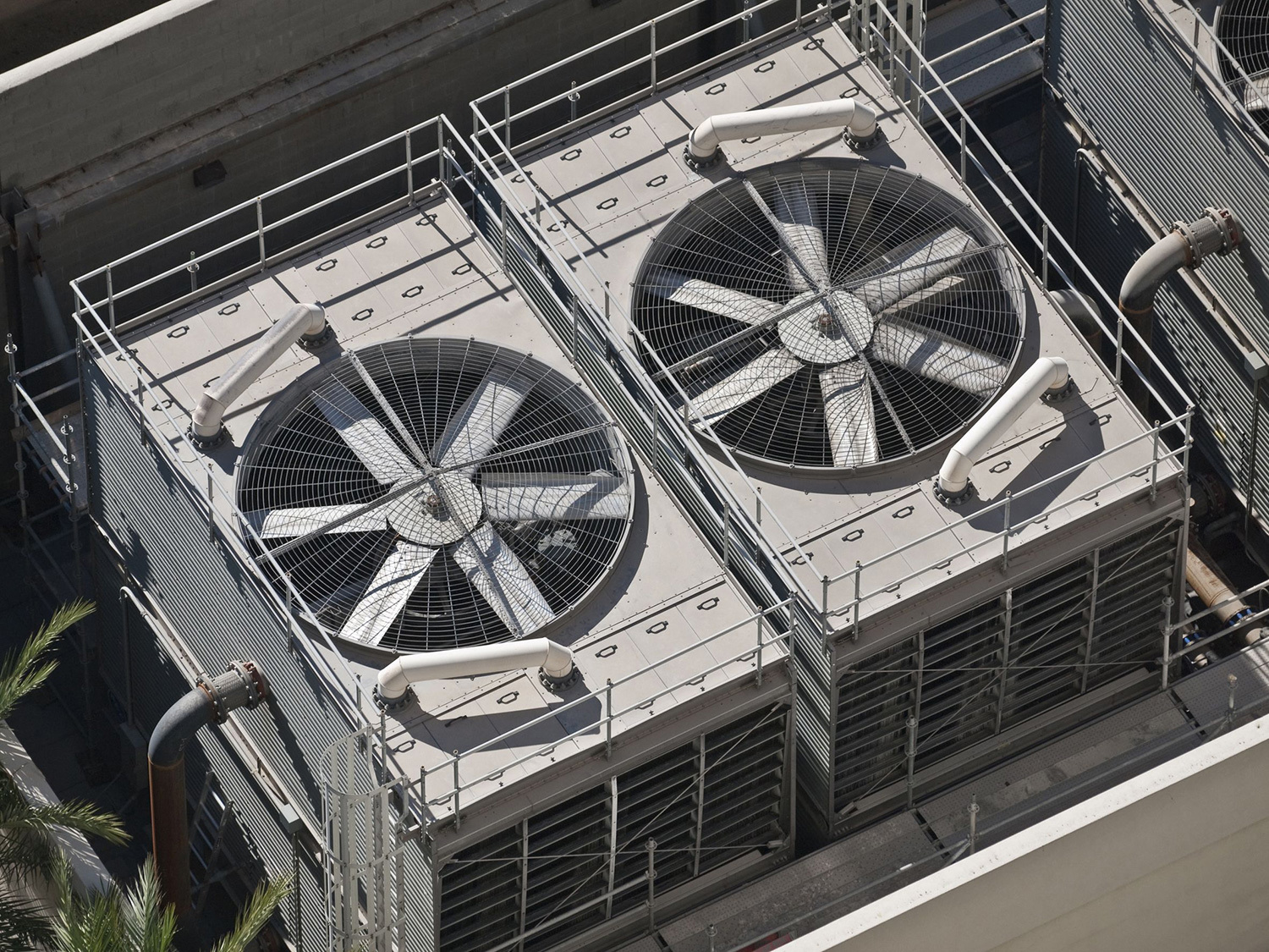 Two large industrial cooling fans on a rooftop, surrounded by safety railings.