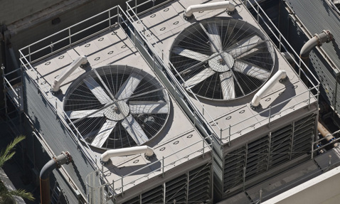 Two large industrial cooling fans on a rooftop, surrounded by safety railings.