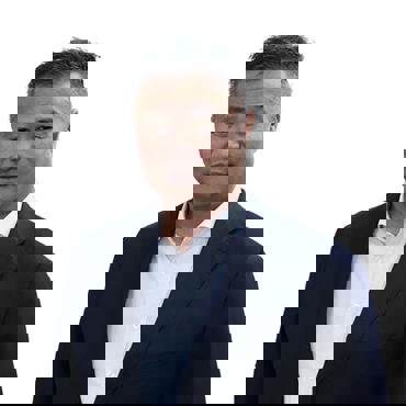 Man in a dark suit and white shirt on a plain background.