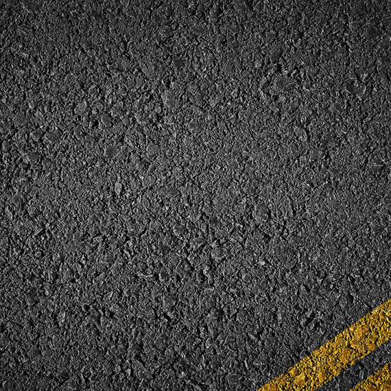 Asphalt road surface with two diagonal yellow lines on the bottom right.
