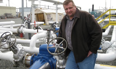 Man standing next to industrial piping and valves in an outdoor facility.