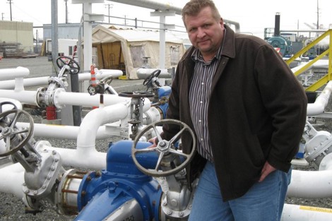 Man standing next to industrial piping and valves in an outdoor facility.