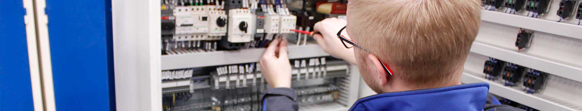 Tekniker som arbetar med en elektrisk kontrollpanel med olika brytare och kablar.