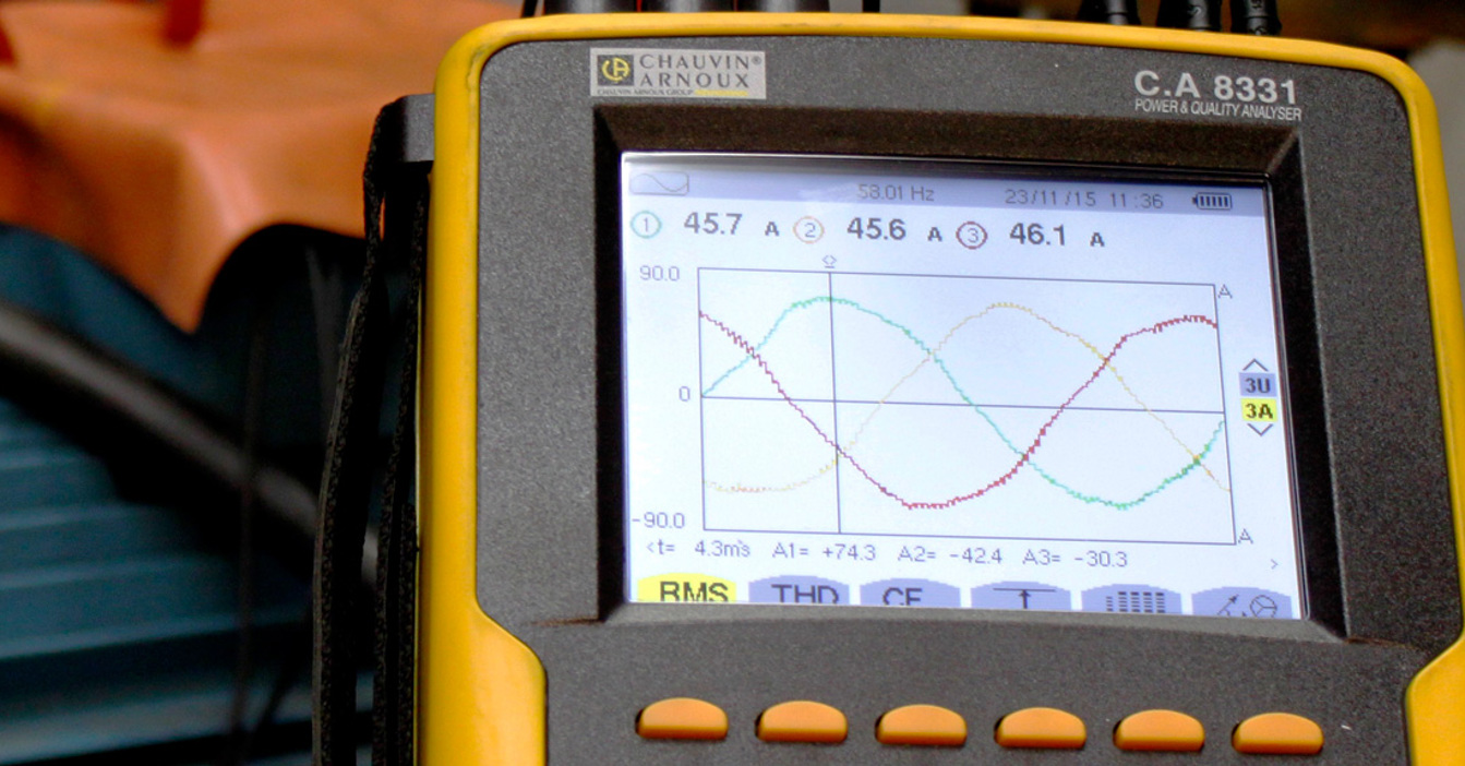 Yellow power quality analyzer displaying waveforms near industrial equipment.