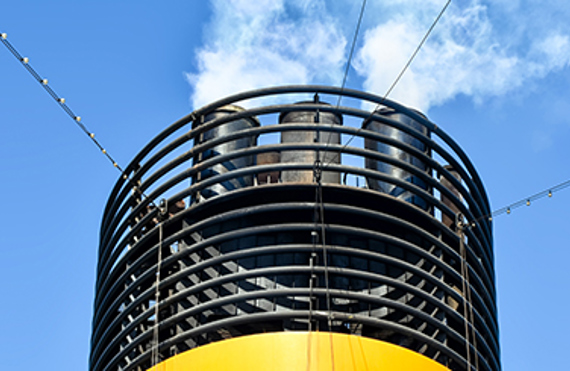 Ship exhaust stacks emitting smoke against a clear blue sky.