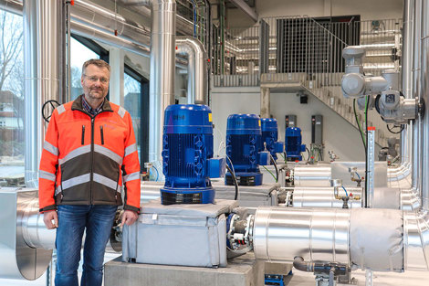 Man in safety gear standing next to DESMI pumps in an industrial facility.