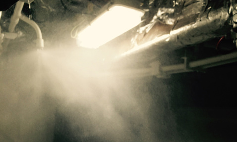 Klar industriell belysning lyser upp dimma från rör ovanför i ett svagt upplyst område.