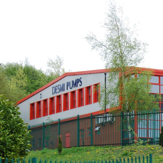 DESMI Pumps building with red accents, surrounded by greenery and a fence.
