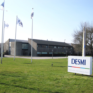 DESMI building with flags and sign on a grassy lawn.