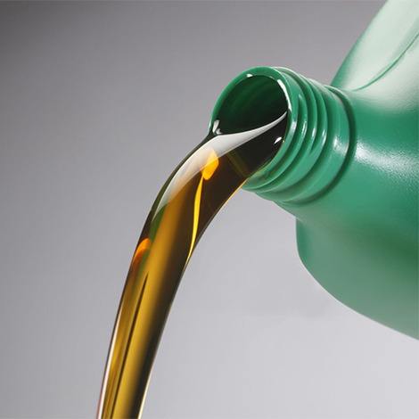 Pouring golden liquid from a green plastic bottle against a gray background.