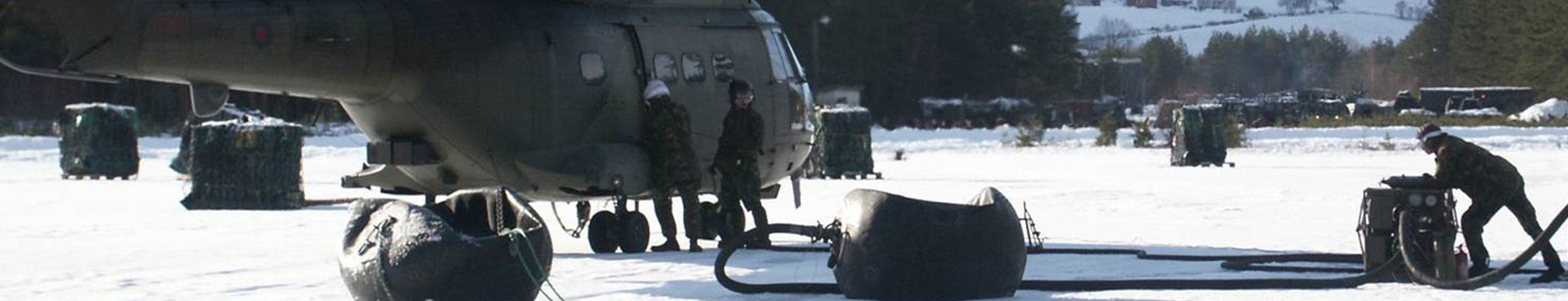 军用直升机在积雪覆盖的场地上进行加油，旁边有士兵和设备。