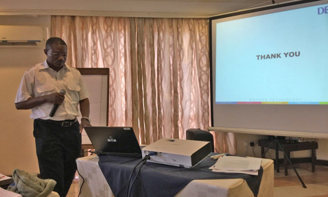 Man presenting with microphone, laptop, and projector screen displaying "Thank You."