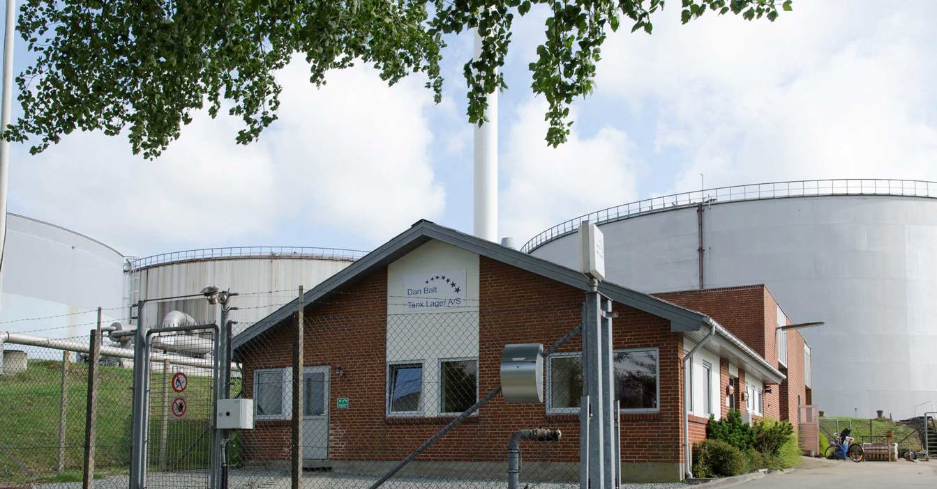 Industrial facility with brick building and large storage tanks, surrounded by fencing.