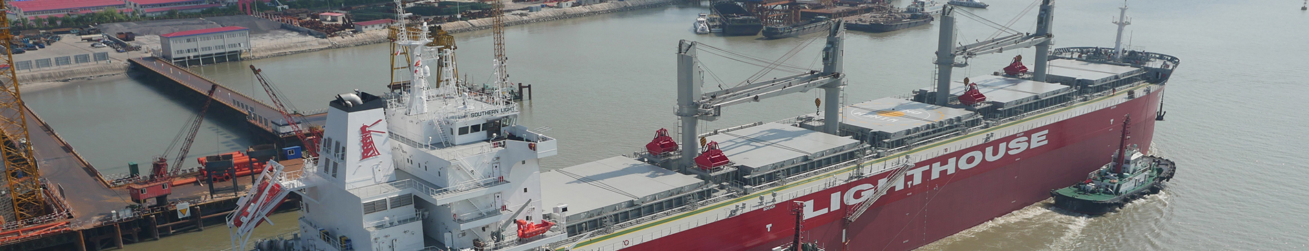 Cargo ship "Lighthouse" docked at an industrial port with cranes and tugboat.