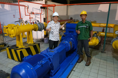 Two workers give thumbs up beside industrial pump in a mechanical room.