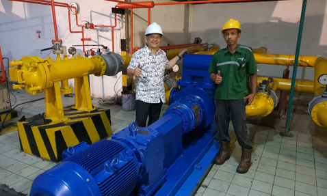 Two workers give thumbs up beside industrial pump in a mechanical room.