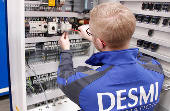 Technician in DESMI uniform working on electrical control panel wiring.