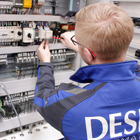 Technician in DESMI uniform working on electrical control panel wiring.