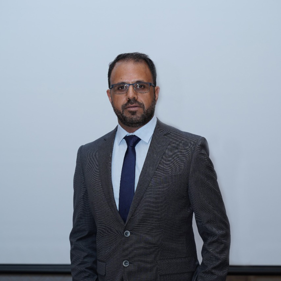 Man in a suit and tie standing against a plain background.