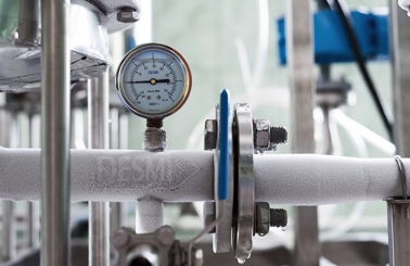 Frozen industrial pipe with DESMI pressure gauge, indicating fluid handling system conditions.