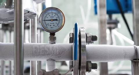 Frozen industrial pipe with DESMI pressure gauge, indicating fluid handling system conditions.