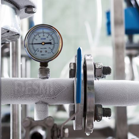Frozen industrial pipe with DESMI pressure gauge, indicating fluid handling system conditions.